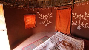 Una habitación con techo de paja, una cama con colcha estampada y una pared con diseño de hojas.