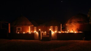 Una hilera de cabañas con techo de paja y ventanas y puertas iluminadas, lo que sugiere una entrada acogedora.