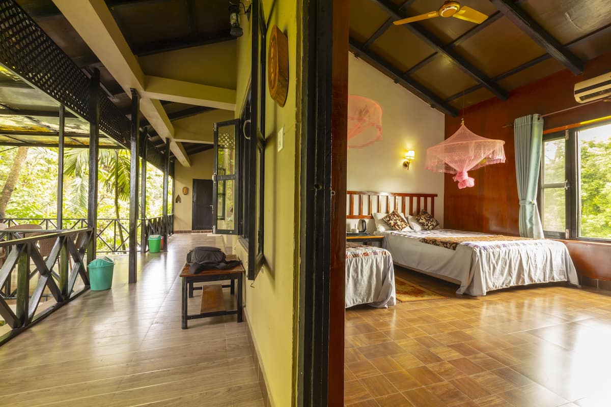 Una habitación con cama, mesita de noche, mesa y ventana con vista a vegetación.