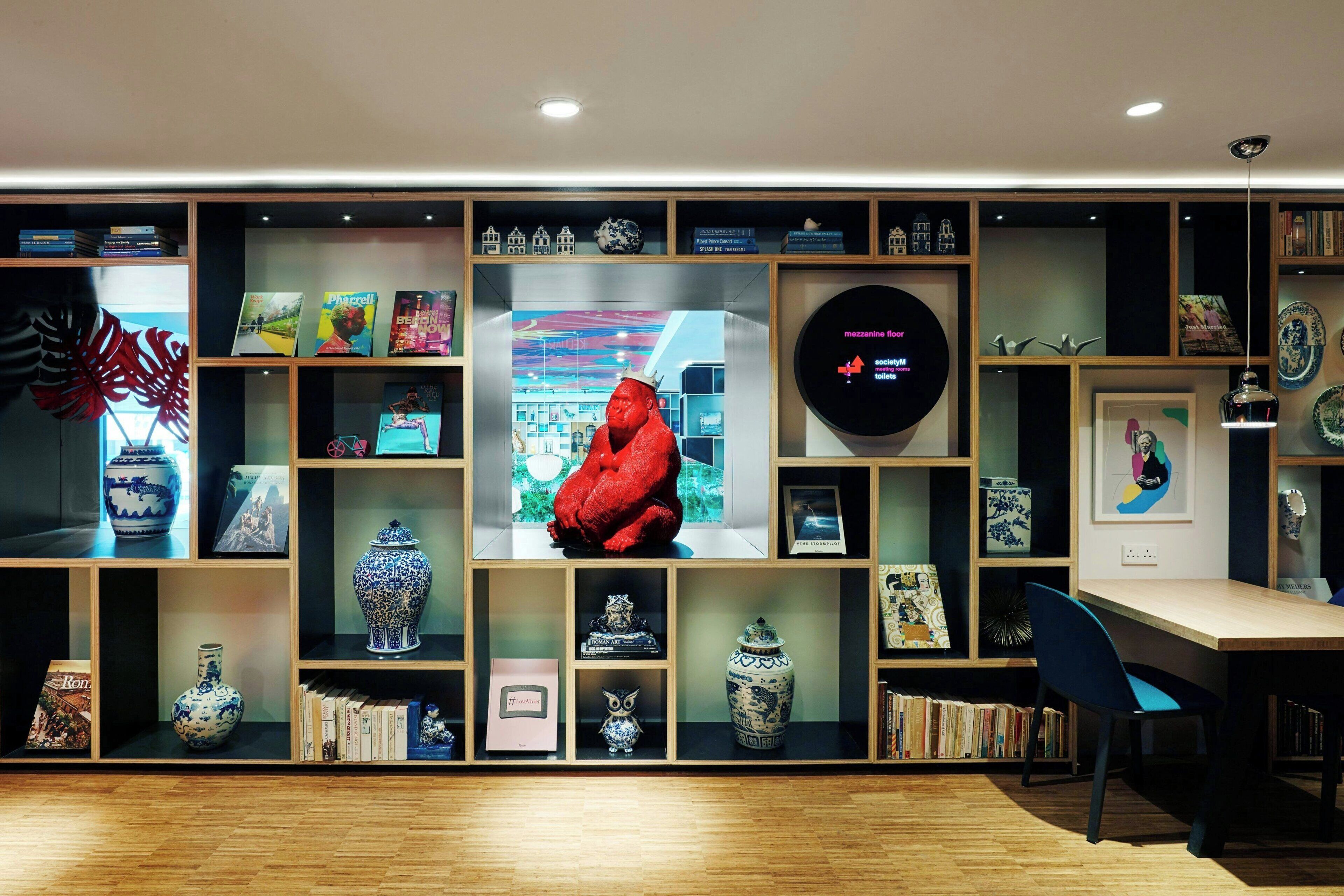 Un interior moderno con estanterías de madera que exhiben libros, objetos decorativos y una gran escultura roja.