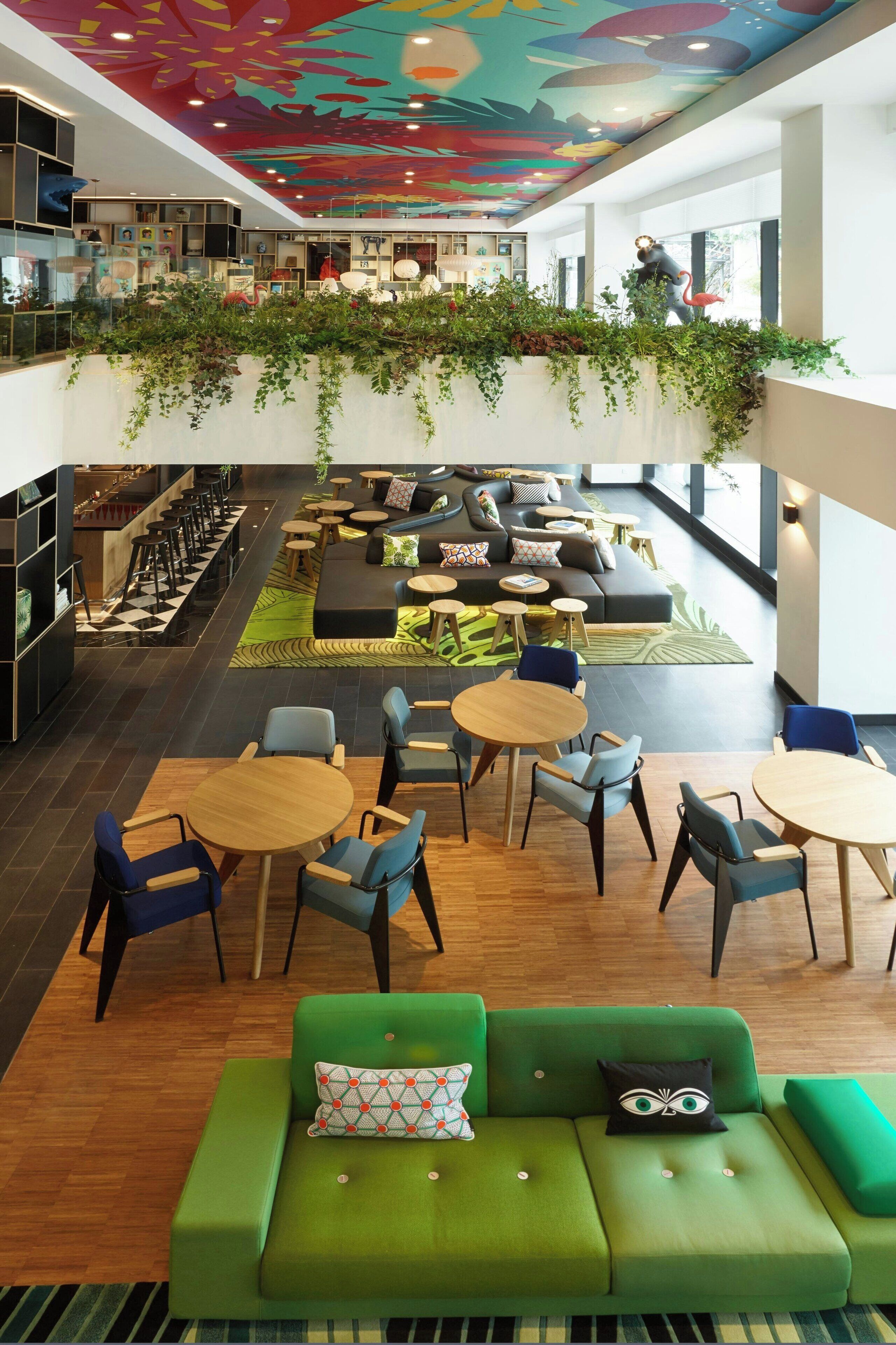 A spacious indoor area with a green sofa, multiple seating arrangements, and a ceiling with a colorful mural.