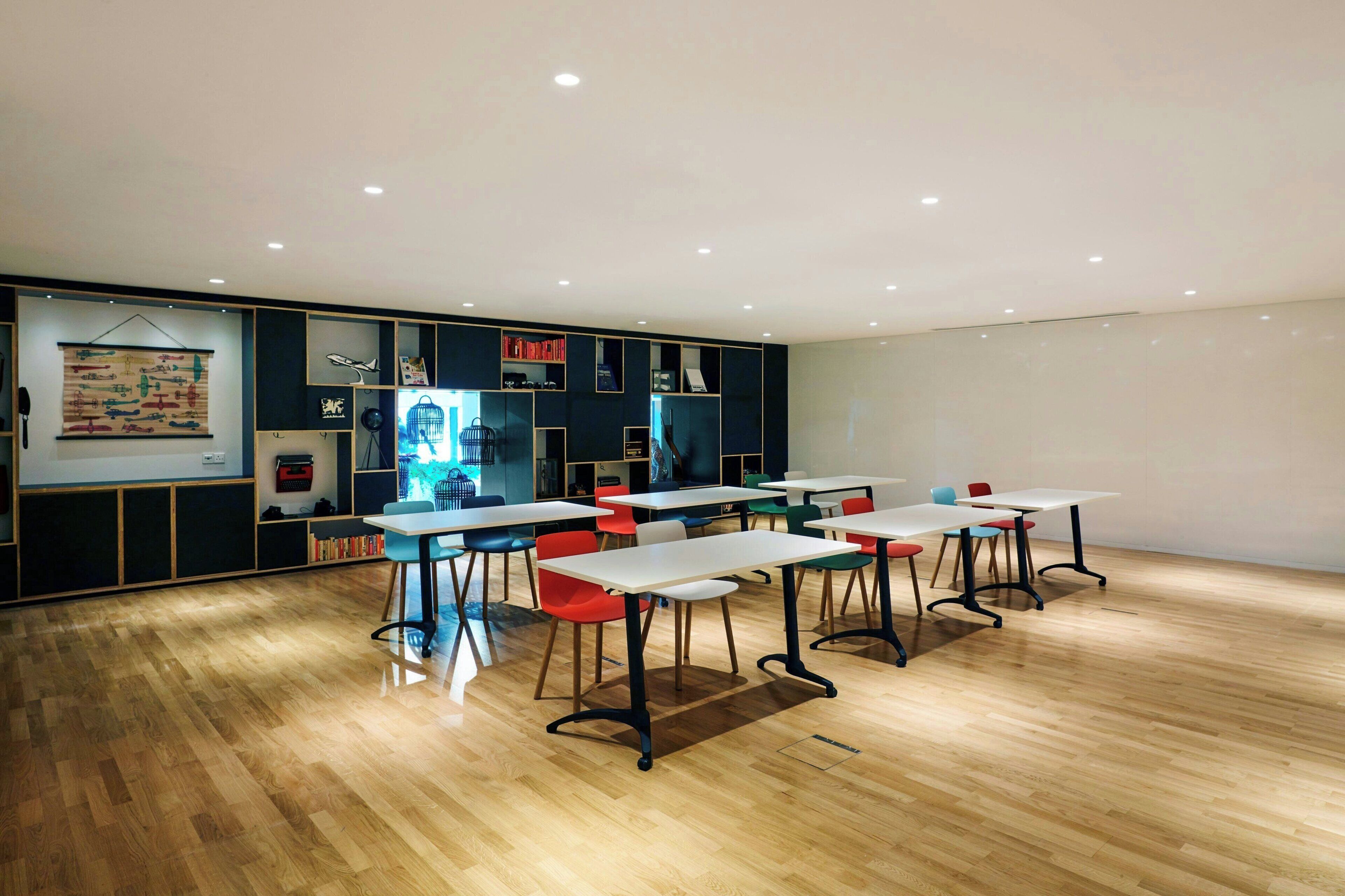 Un comedor moderno con suelo de madera, mesas blancas y sillas coloridas.