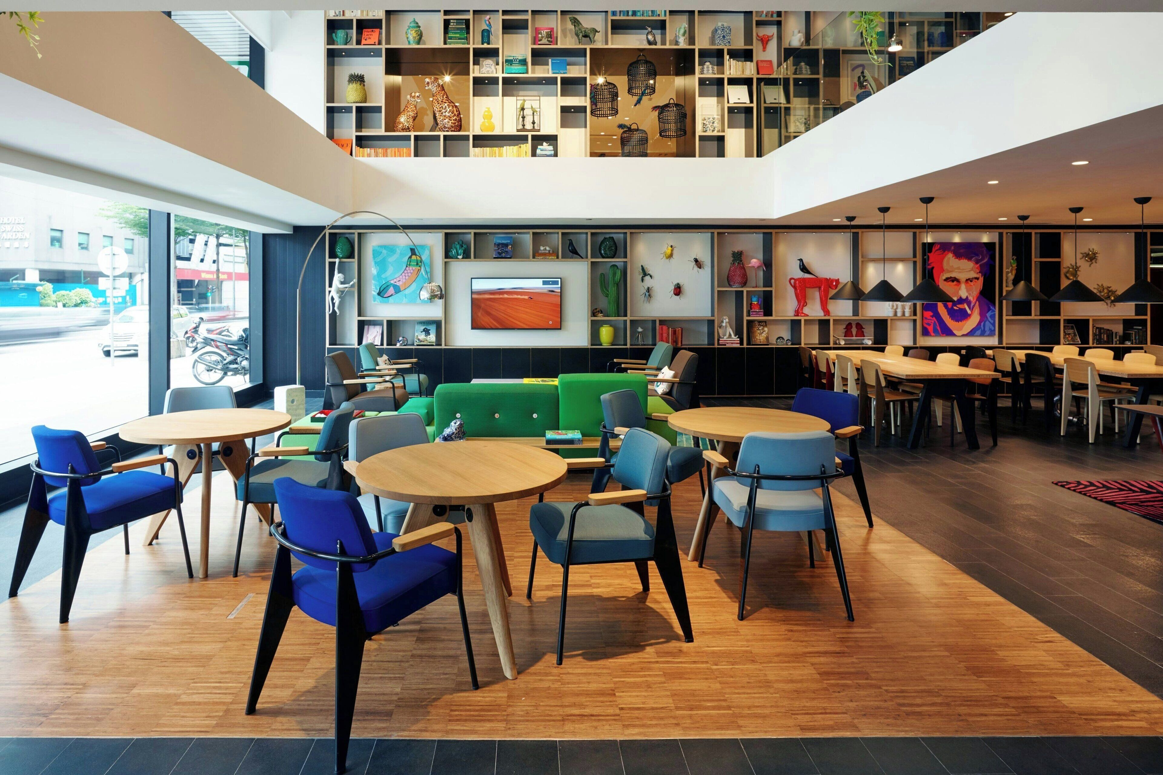 Ein modernes Interieur mit einer zentralen grünen Sitzgruppe, mehreren Tischen und verschiedenen Dekorationen auf Regalen.