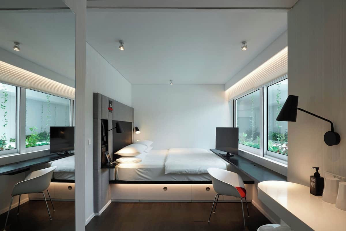 Een moderne slaapkamer met een bed, bureau, stoel en grote ramen.