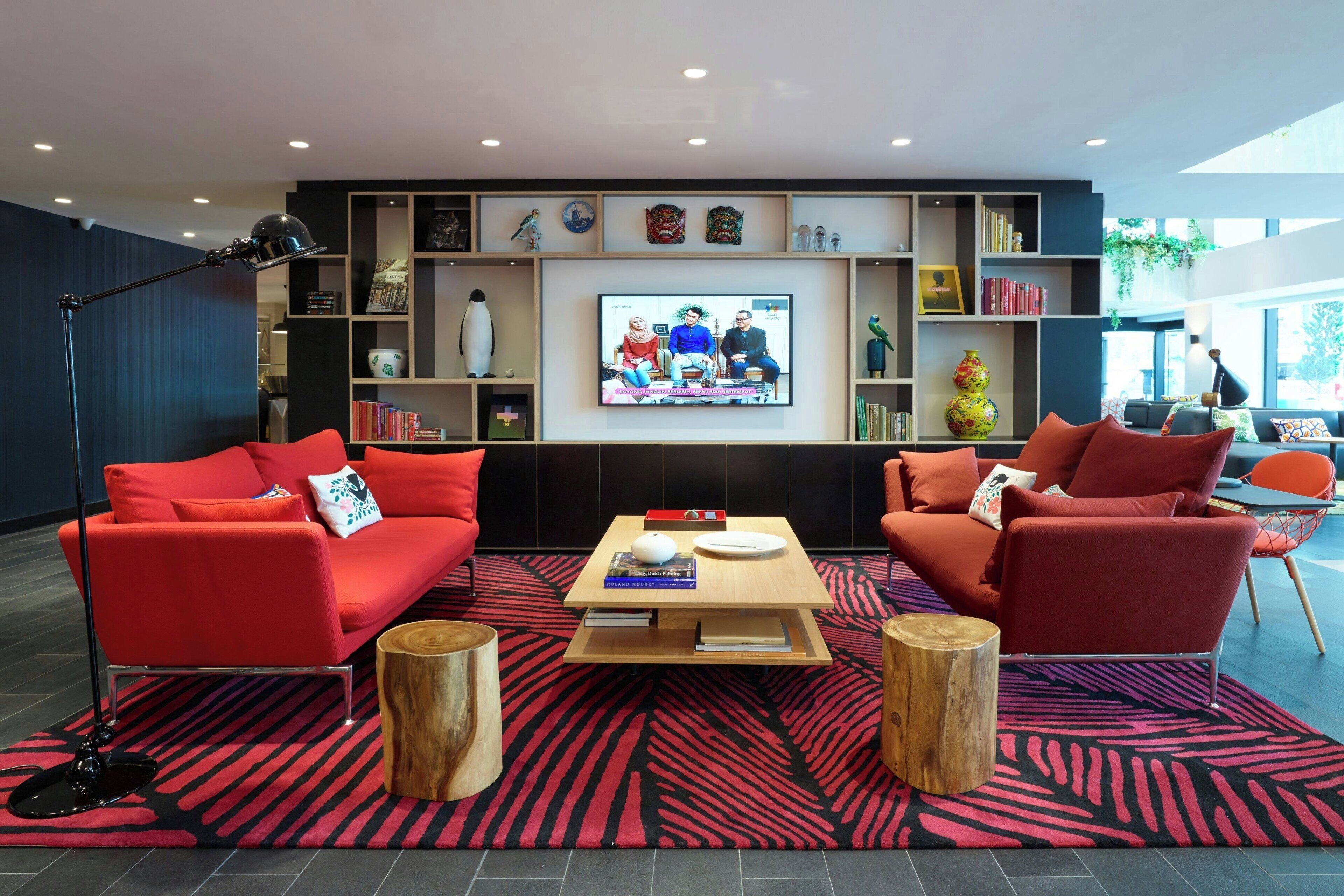 A modern living room with red sofas, a wooden coffee table, and a large flat-screen TV mounted on the wall.
