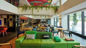 A modern lounge area with green sofas, a bar, and a ceiling mural.