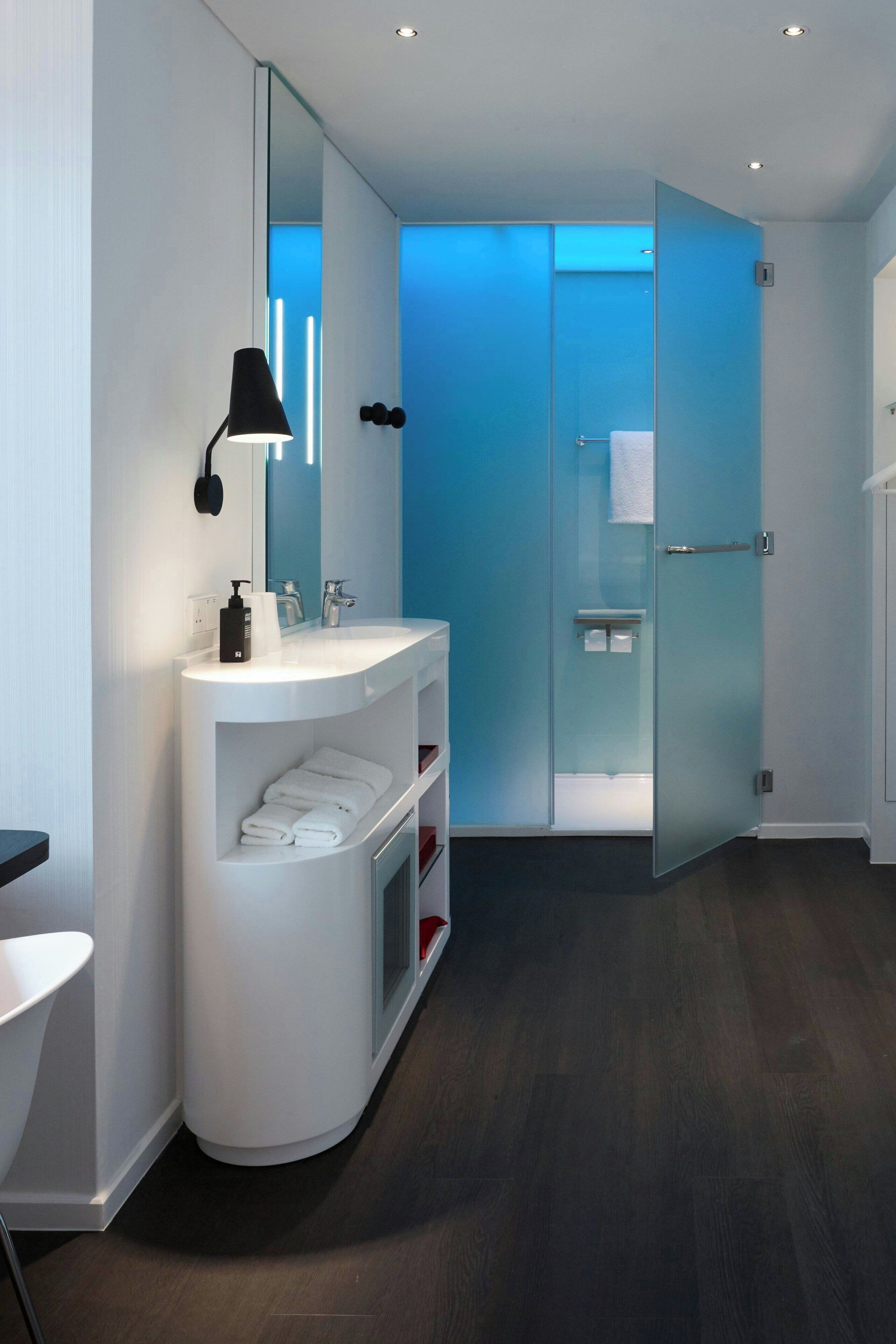 A modern bathroom with a white vanity, a glass-enclosed shower, and a blue-lit glass door.