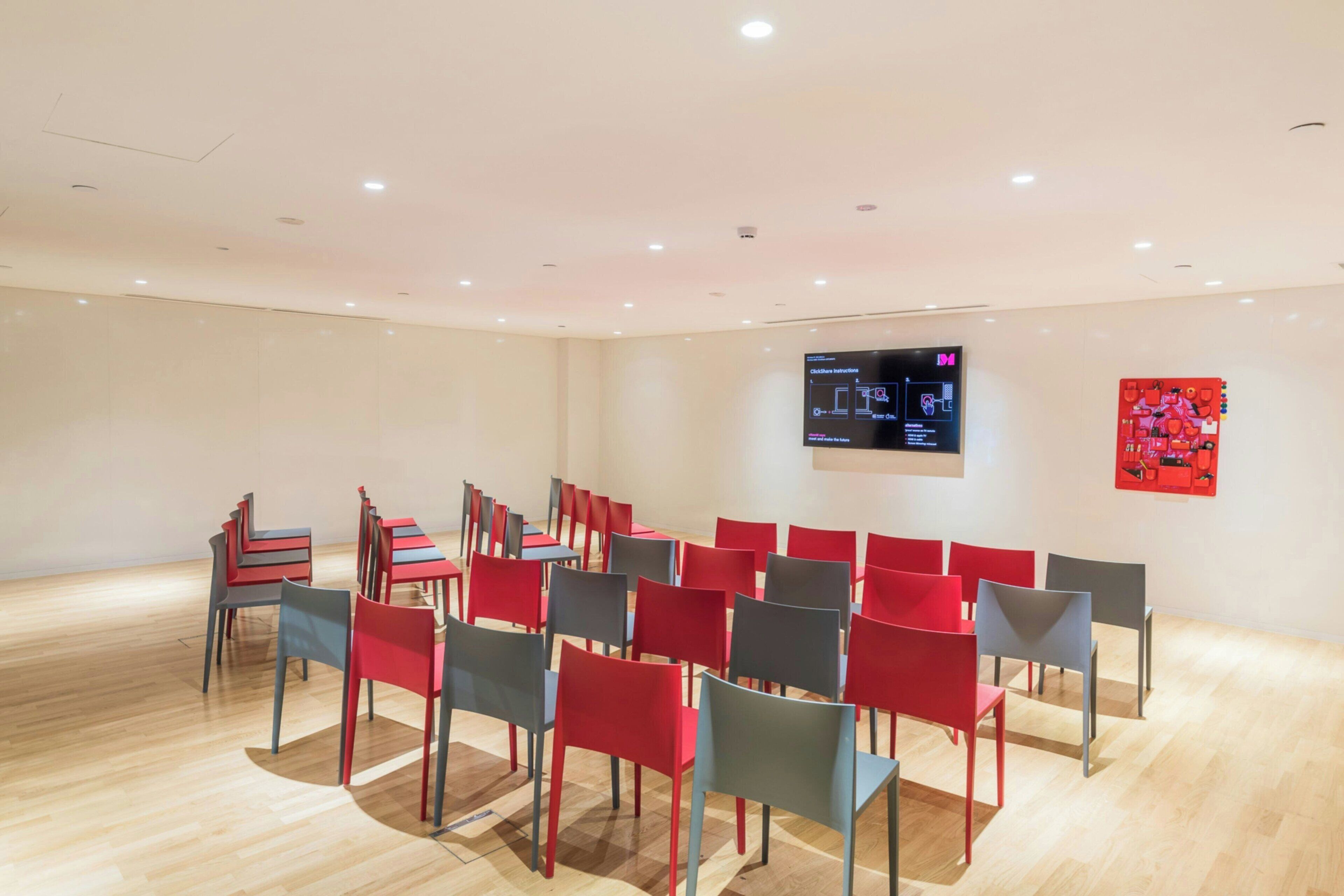 A conference room with rows of chairs and a large screen on the wall.