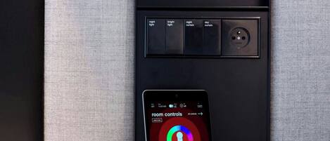A control panel with a smartphone displaying room controls, a power outlet, and a red button.