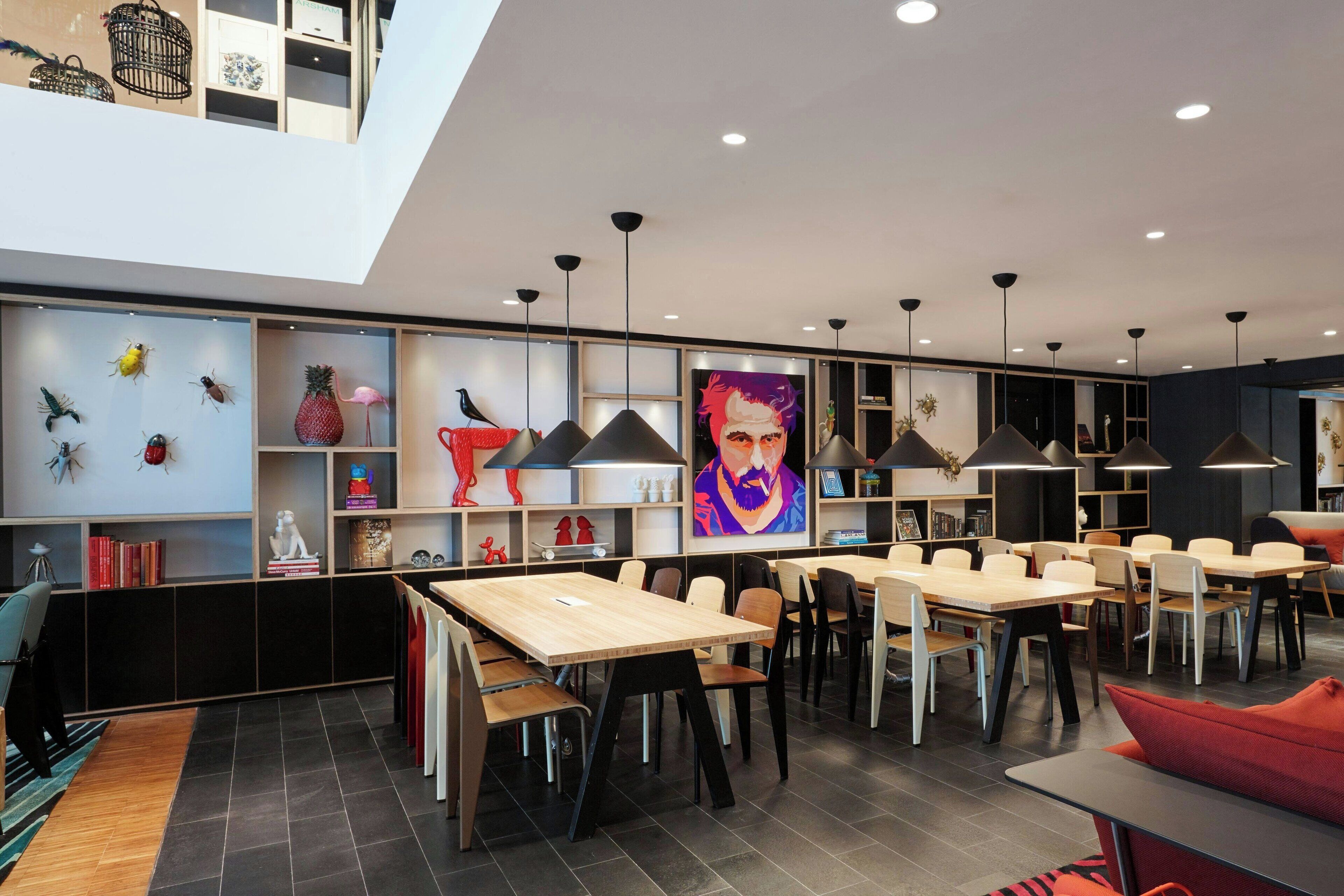 A modern dining area with multiple tables and chairs, a high ceiling with recessed lighting, and decorative items on shelves.