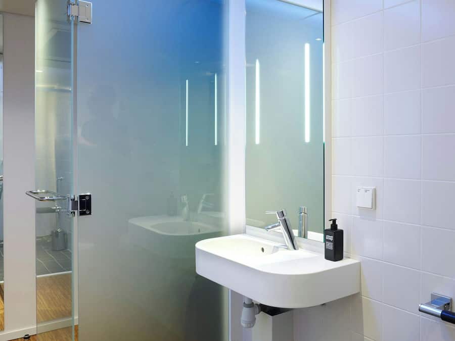 Une salle de bain moderne avec une douche à parois de verre, un lavabo blanc et un grand miroir.