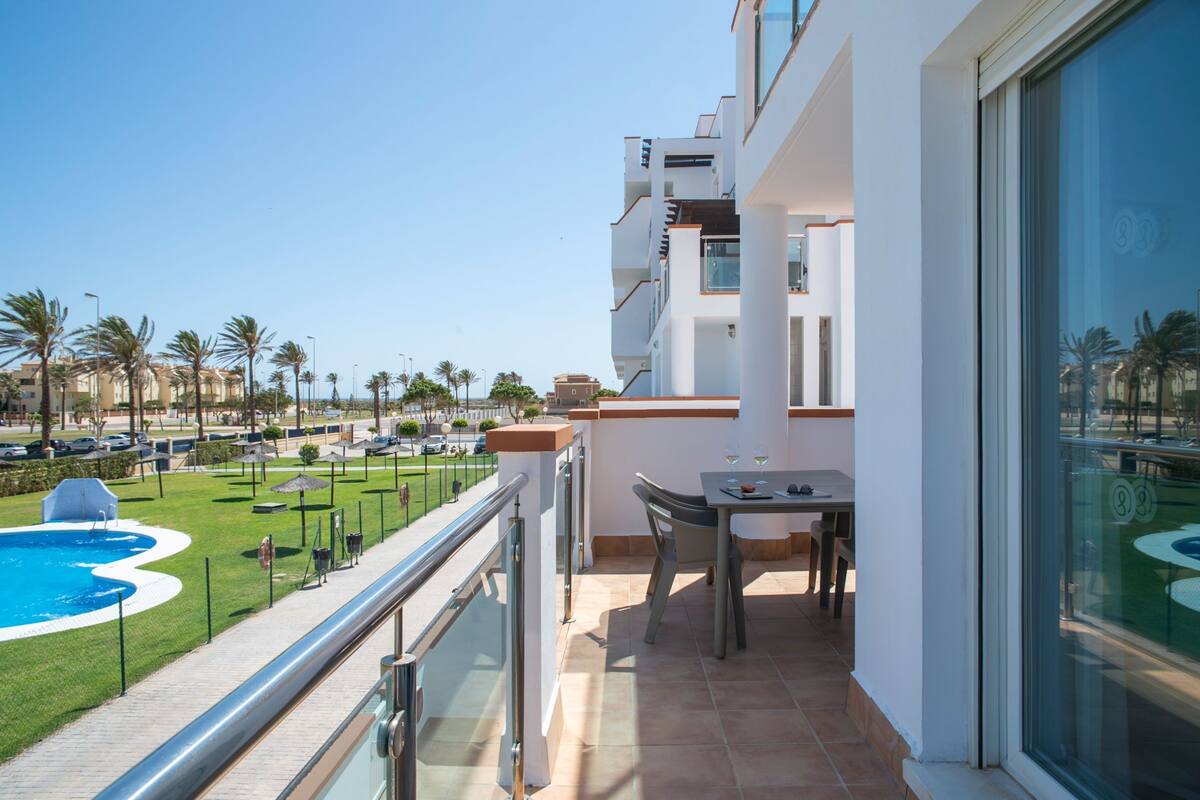 A balcony with a table and chairs, overlooking a swimming pool and palm trees.