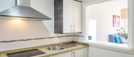 A modern kitchen with a built-in stove, stainless steel sink, and a window overlooking a living area.