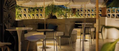 An outdoor seating area with tables and chairs, striped umbrellas, and potted plants.