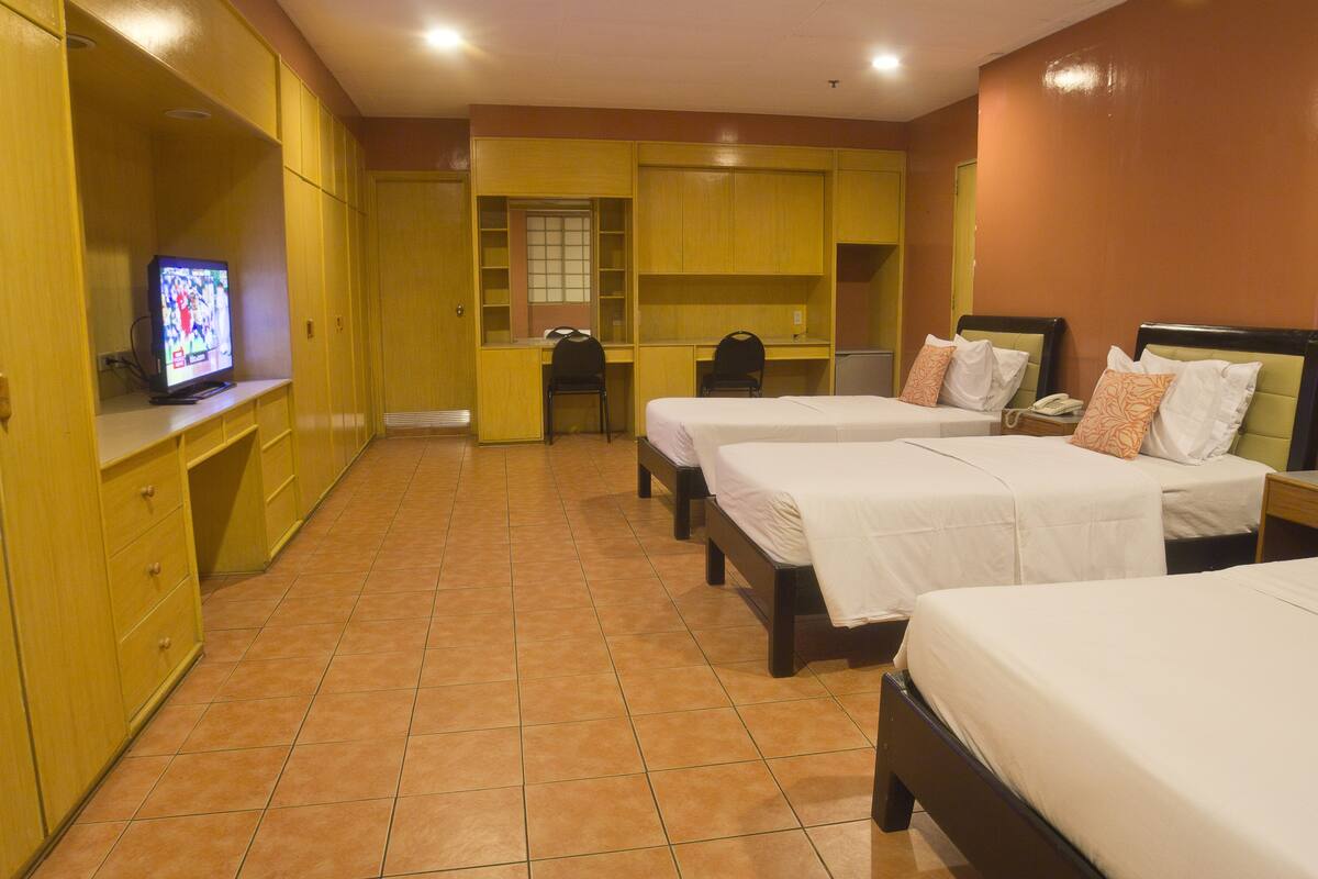 A hotel room with three beds, a desk, a television, and a wardrobe.