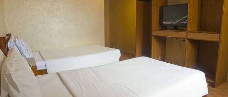 A hotel room with two single beds, a wooden wardrobe, and a television on a shelf.