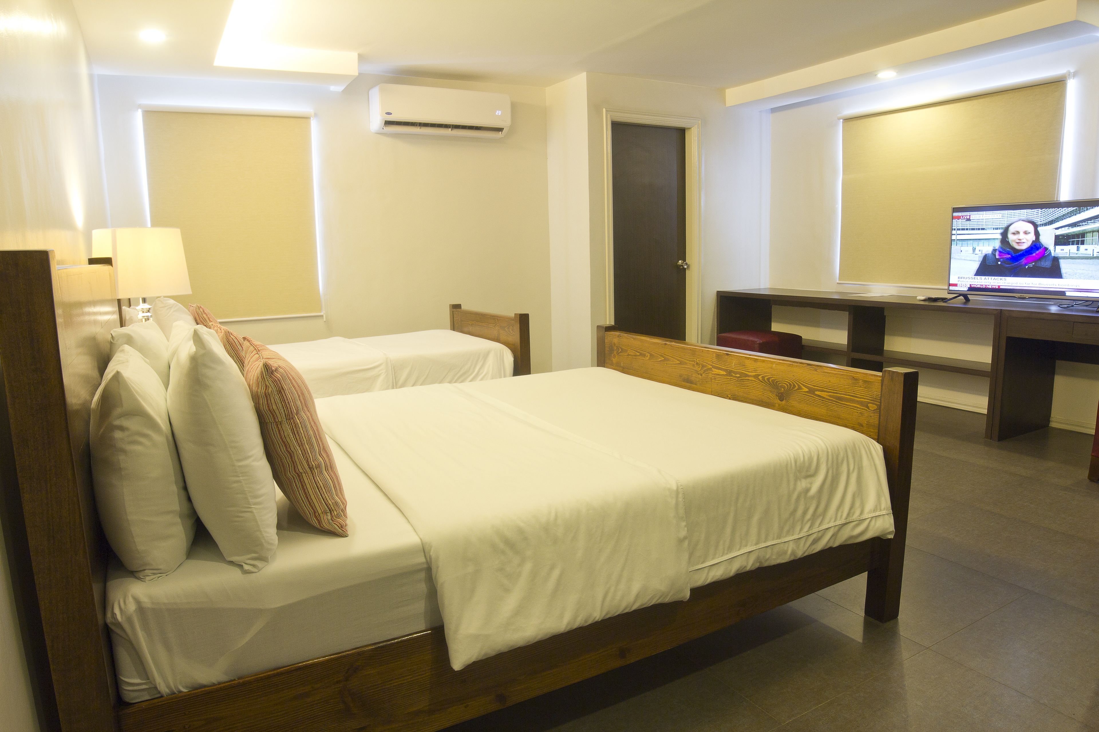 A hotel room with two beds, a desk, a television, and an air conditioning unit.