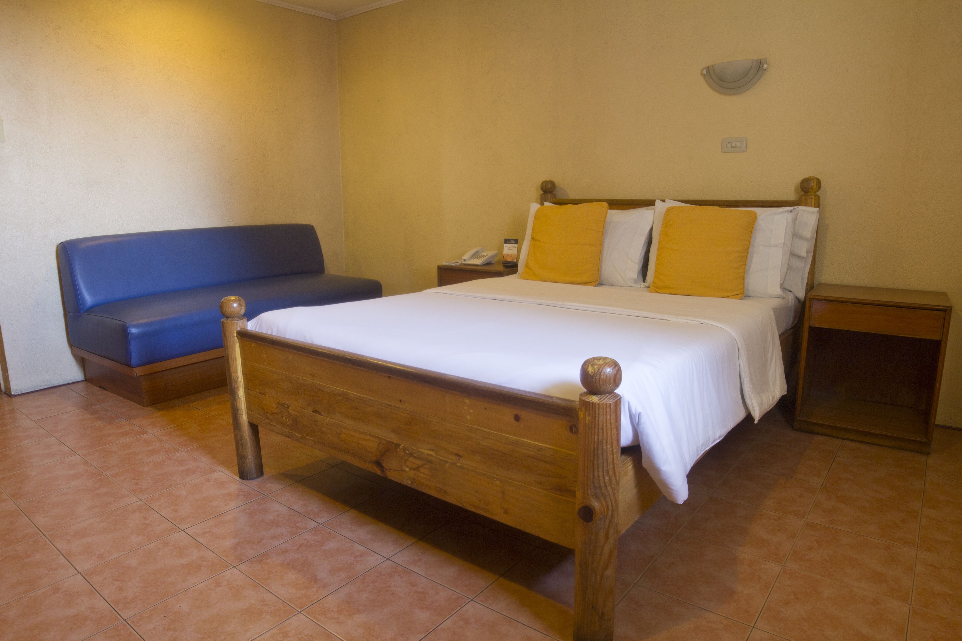 A room with a wooden bed, a blue sofa, and a nightstand with a lamp.