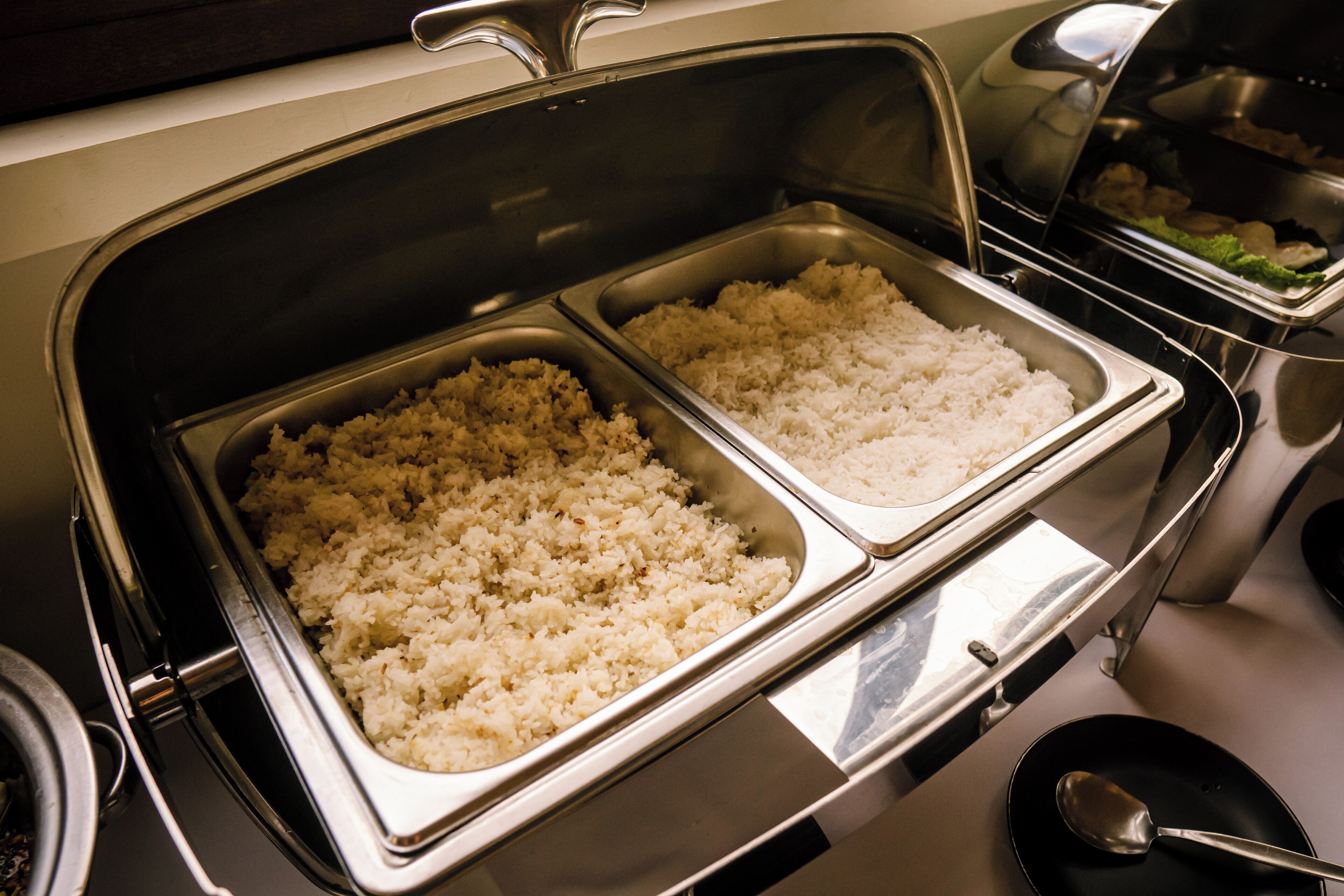 A buffet with two trays of rice and a container of vegetables.