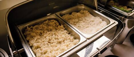 A buffet with two trays of rice and a container of vegetables.