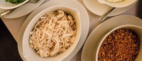 Une table sur laquelle on trouve différents plats, notamment un bol d’œufs coupés en tranches, un bol de poulet effiloché et un bol d’oignons verts hachés.