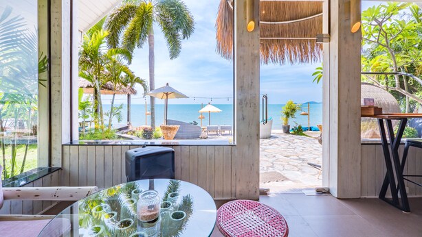 A beachside room with a glass table, wicker chair, and a view of the ocean. - Sea Valley Resort (Koh Samui)
