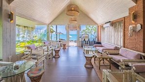 A spacious, open-plan lounge area with a high ceiling, large windows offering a view of the sea, and a variety of seating arrangements including sofas, chairs, and tables. - Sea Valley Resort (Koh Samui)