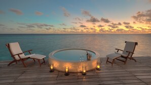 Una terraza de madera con un jacuzzi circular, dos sillones de lounge y velas.