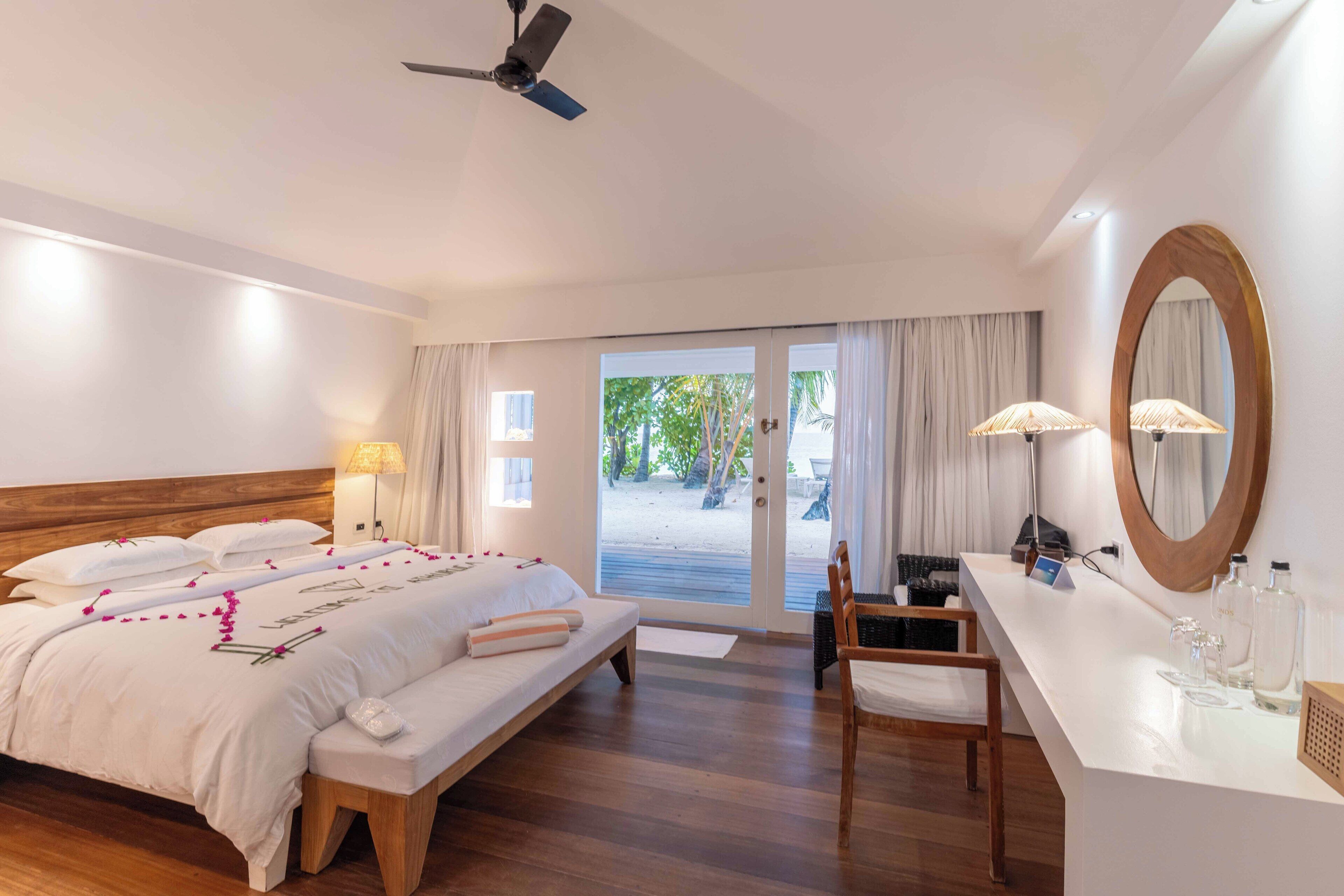 A hotel room with a bed, bedside table, chair, and a large mirror.