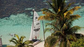 A sailboat with a sail marked "680 HOBIE CAT" on a beach with clear turquoise water and palm trees.