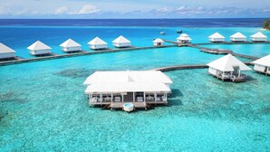Bungalows sobre el agua con aguas turquesas cristalinas, pasarelas de madera y una piscina central.