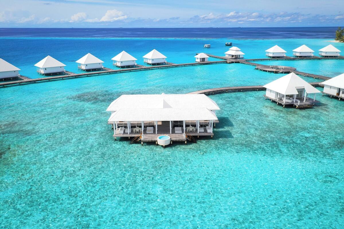 An overwater bungalows with clear turquoise water, wooden walkways, and a central pool.