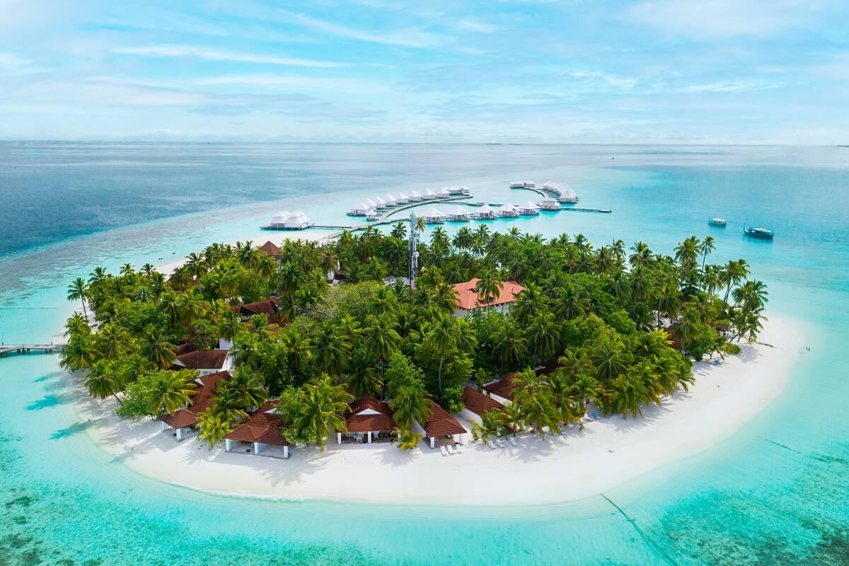 An aerial view of a tropical island resort with overwater bungalows, a white sandy beach, and clear turquoise waters.