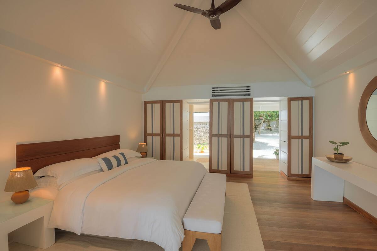 A bedroom with a large bed, bedside tables, a ceiling fan, and a view of the outside.