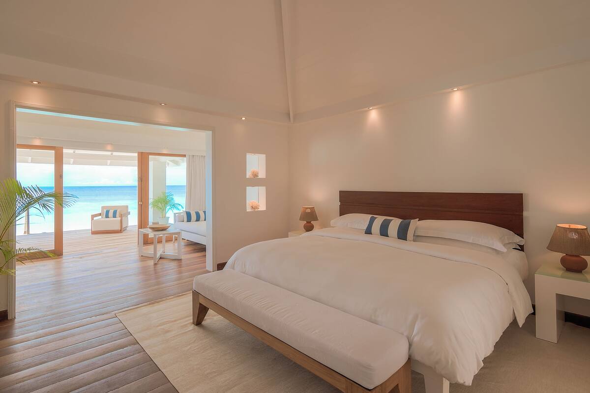A spacious bedroom with a large bed, a wooden headboard, and a view of the ocean through an open door.