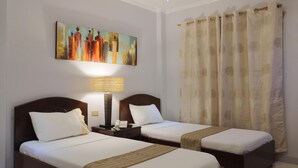 A hotel room with two beds, a painting on the wall, a lamp, and a curtain.