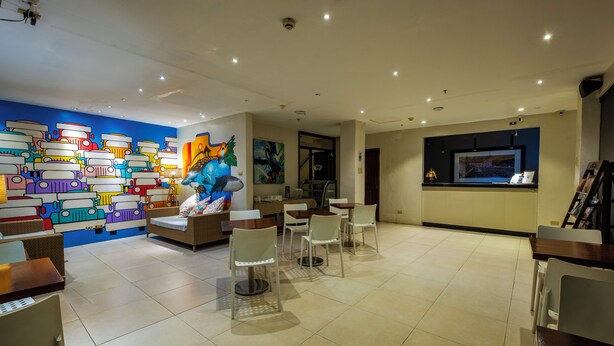 A modern hotel lobby with a colorful mural, seating areas, and a television screen.