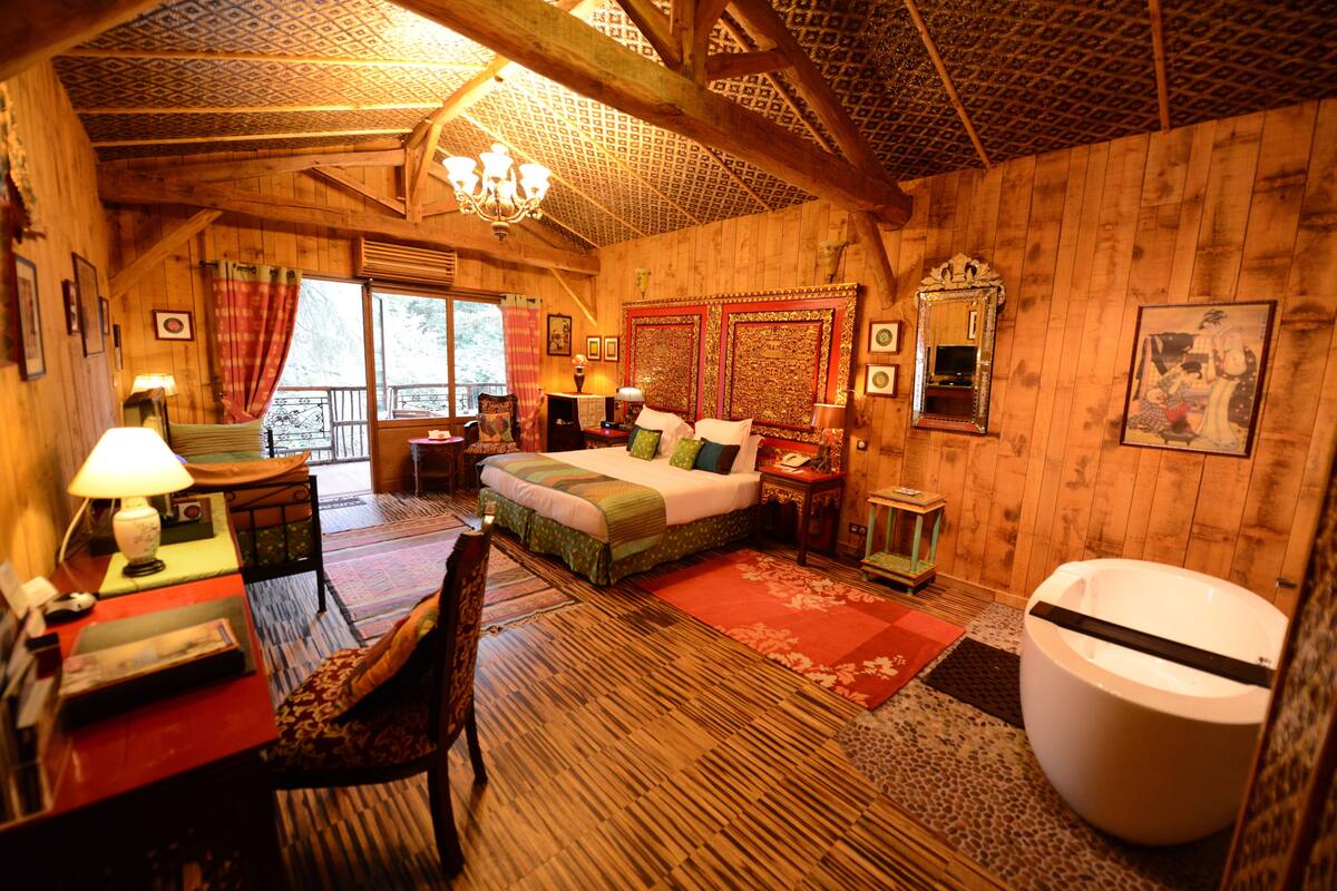 A wooden cabin room with a bed, a desk, a chair, a large mirror, and a bathtub.