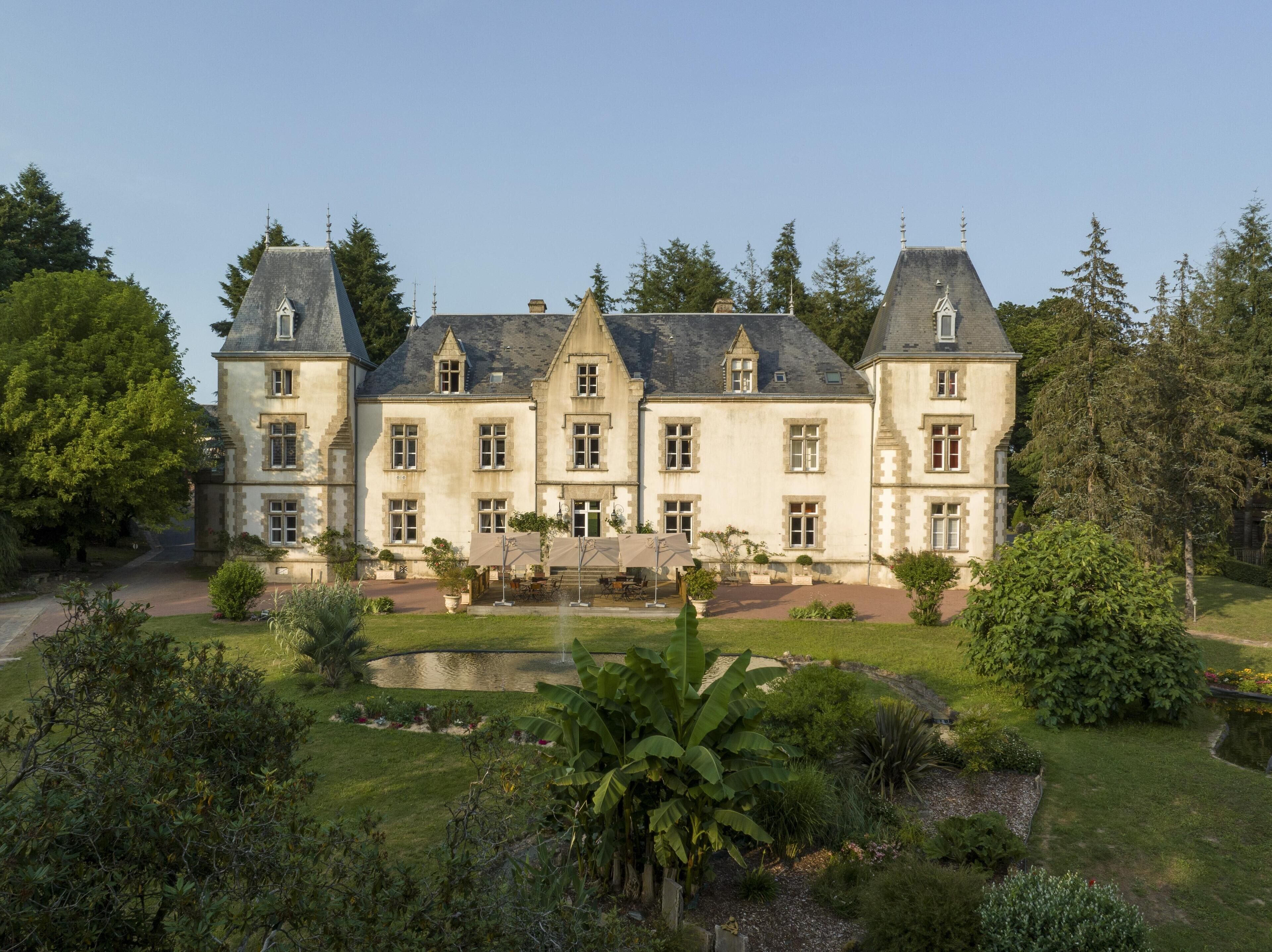 A large, historic building with multiple windows and a symmetrical facade, surrounded by lush greenery and a small pond.