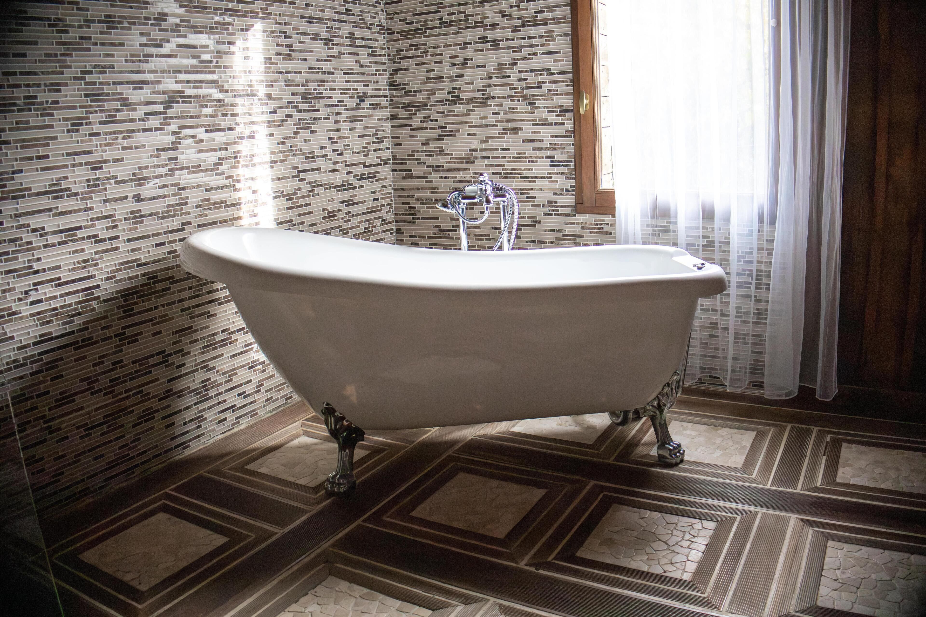 Un baño con bañera independiente, paredes con azulejos y suelo estampado.
