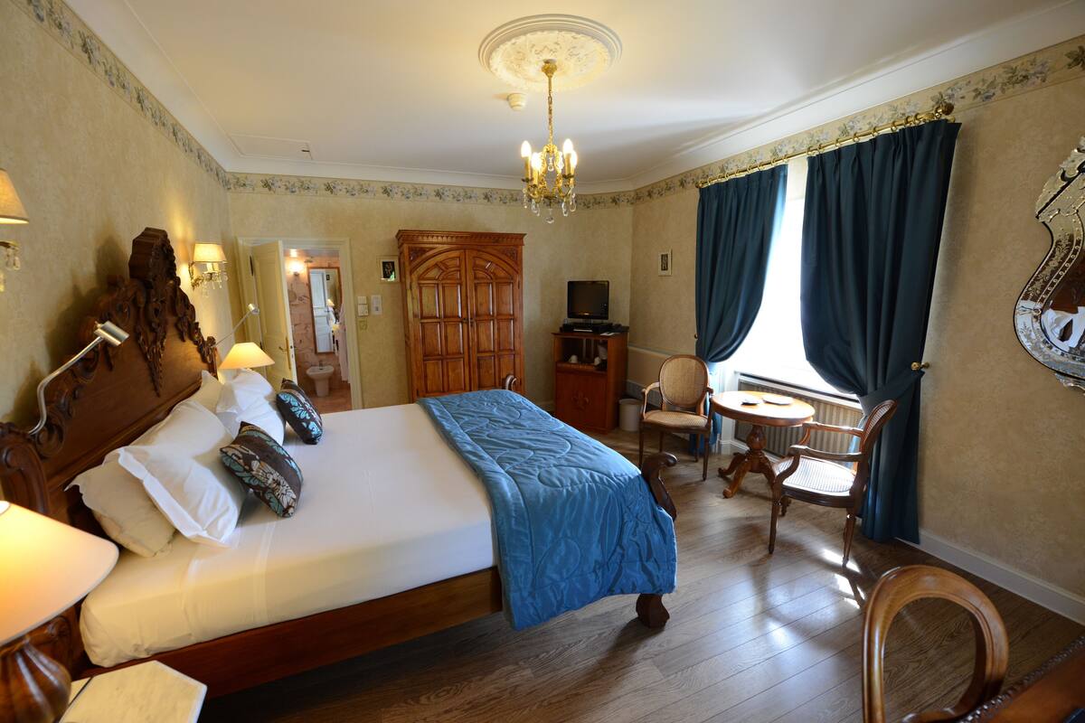 A hotel room with a bed, a desk, a chair, a television, and a window with curtains.
