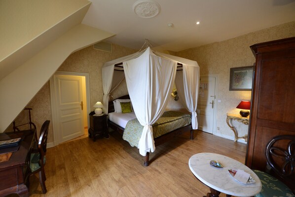 A bedroom with a four-poster bed, a small table, and a chair.