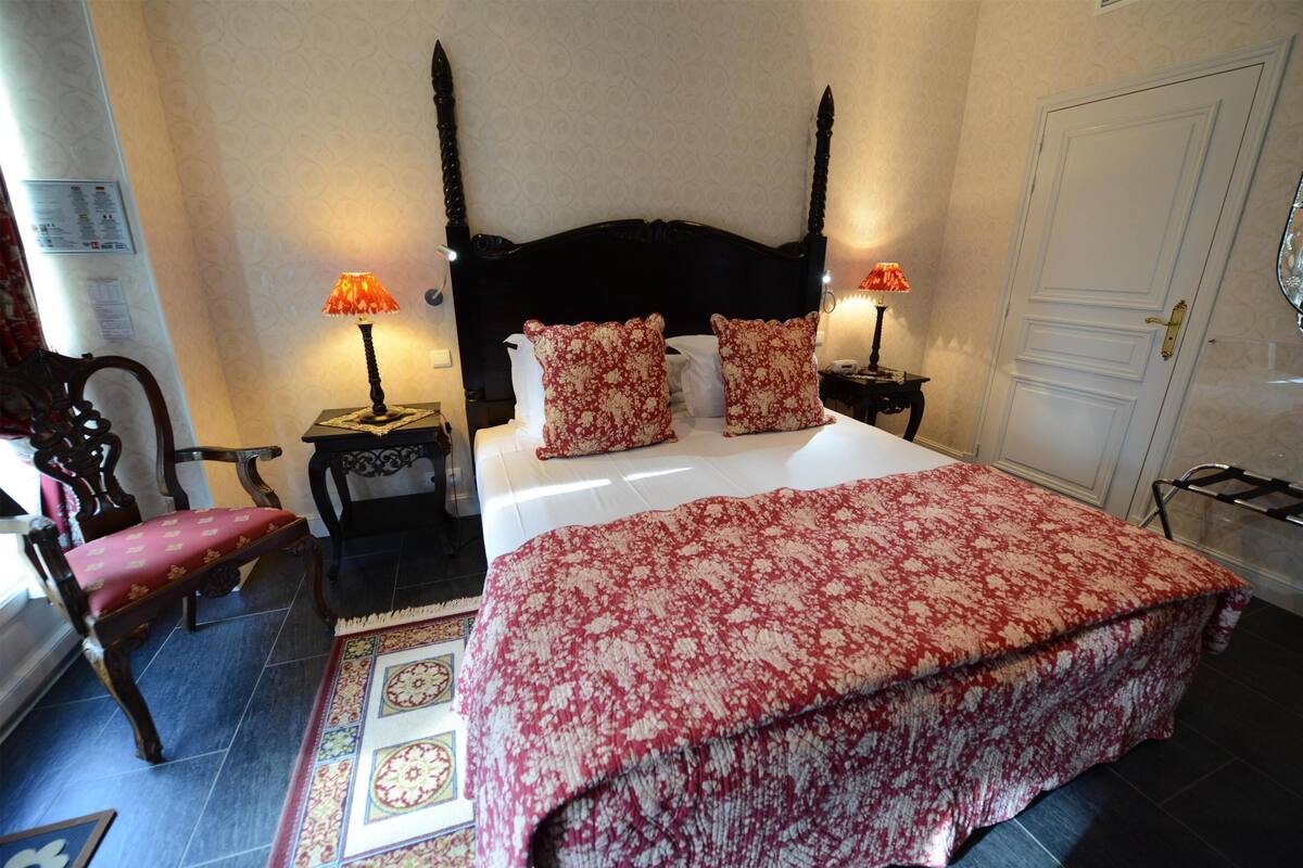 A neatly arranged bedroom with a large bed, two bedside tables with lamps, a chair, and a door.