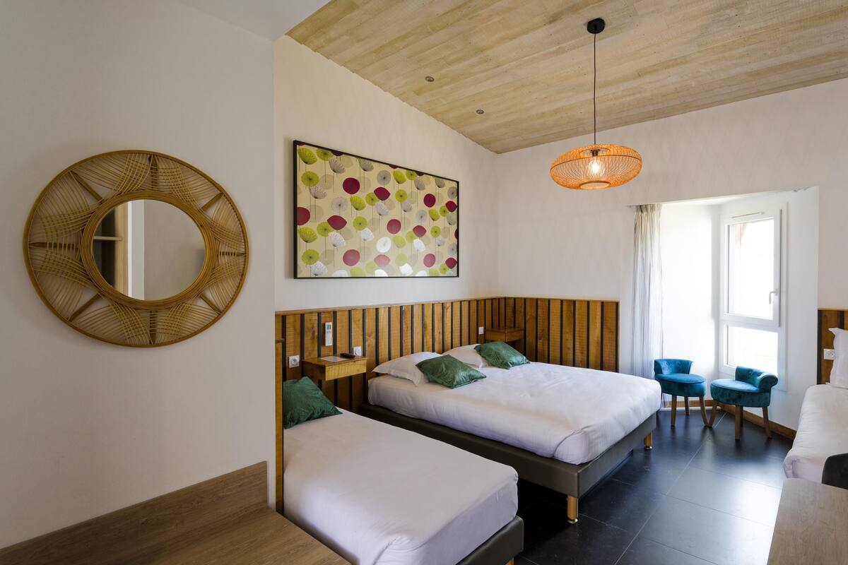 A hotel room with two beds, a wooden ceiling, a large mirror, a colorful artwork, and a hanging light fixture.