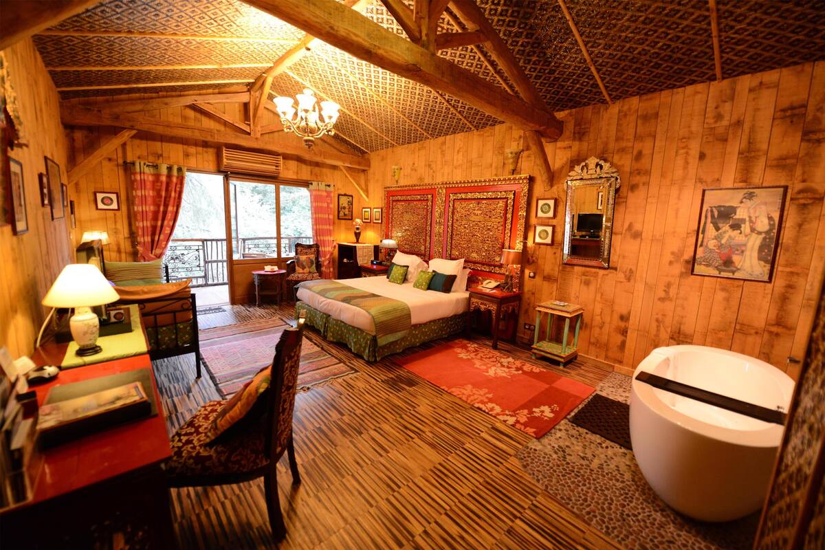 A wooden cabin bedroom with a bed, desk, chair, and a large bathtub.