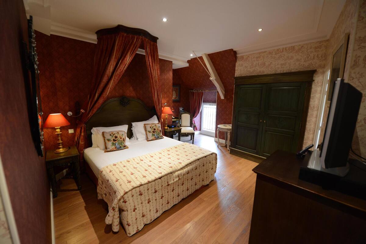 A bedroom with a four-poster bed, a nightstand with a lamp, a dresser, and a television.
