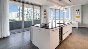 Cozinha moderna com uma ilha grande, armários brancos e vista para edifícios altos.