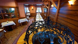 A restaurant with wooden walls, a long table with white tablecloths, and a decorative metal structure in the center. - Hotel Karpatsky Dvor (Lozorno)