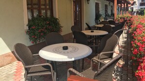 An outdoor seating area with wicker chairs and tables, a covered section with striped awning, and a building with windows and doors. - Hotel Karpatsky Dvor (Lozorno)