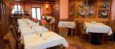 Un restaurante con varias mesas preparadas para comer, sillas de madera y un ventanal decorativo con motivos florales.